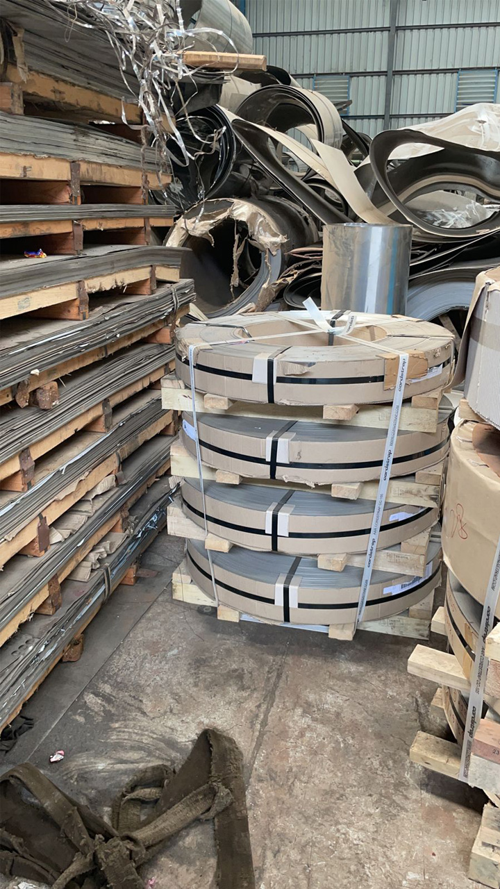 Packed slit coils on a pallet beside stacked stainless steel sheets in the stockyard