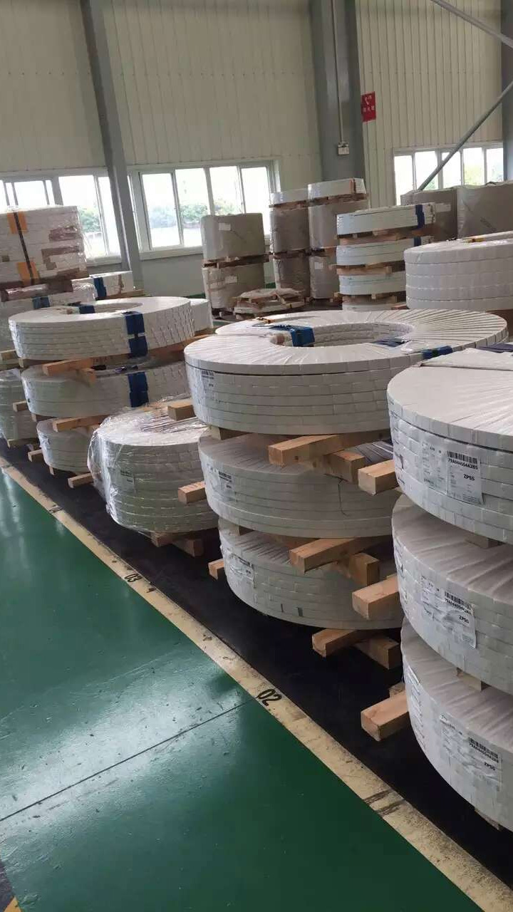 Rows of wrapped stainless steel strip coils stacked on wooden skids in the warehouse